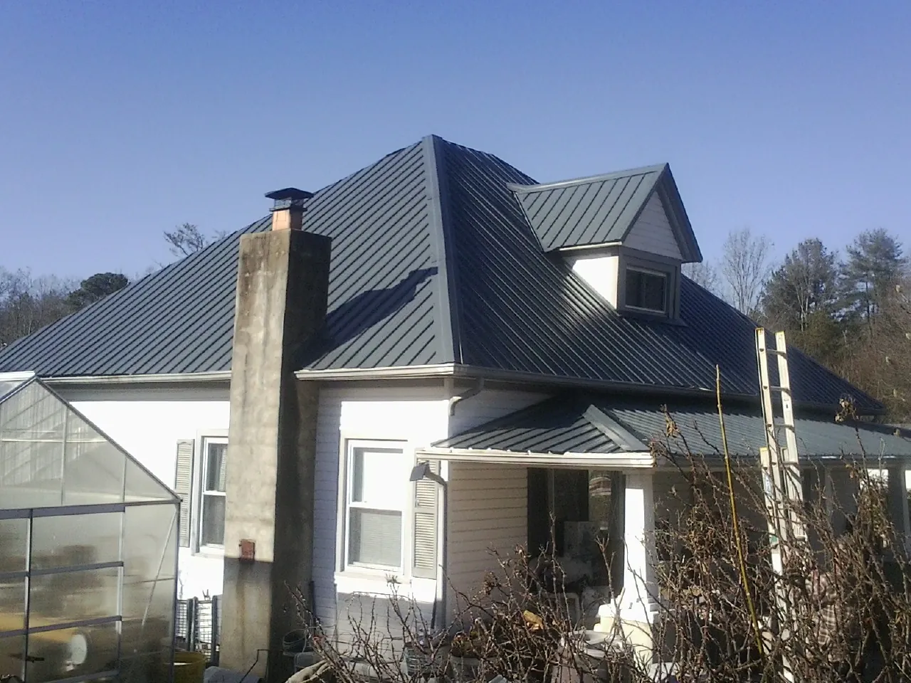 Dark blue standing seam metal roof on a white farmhouse with dormer — Slate & Tile Roof Repair by Roofing Brothers in Clarks Grove