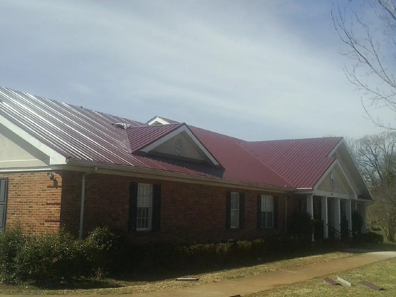 Red metal roof with gabled entries on a long brick building, from a Hail Damage Roof Repair job in Clarks Grove