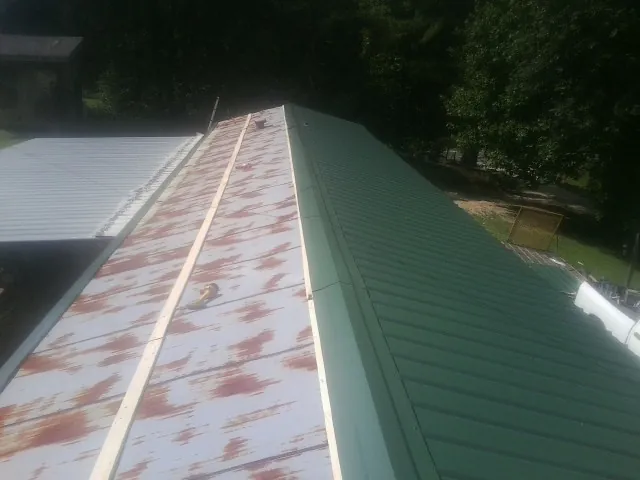 Old rusted panels beside newly installed green metal roofing — Wind Damage Roof Repair by Roofing Brothers in Clarks Grove