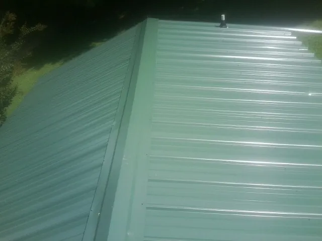 New green metal panels meeting at the ridge of a roof — Flat Roof Repair work by our crew in Clarks Grove