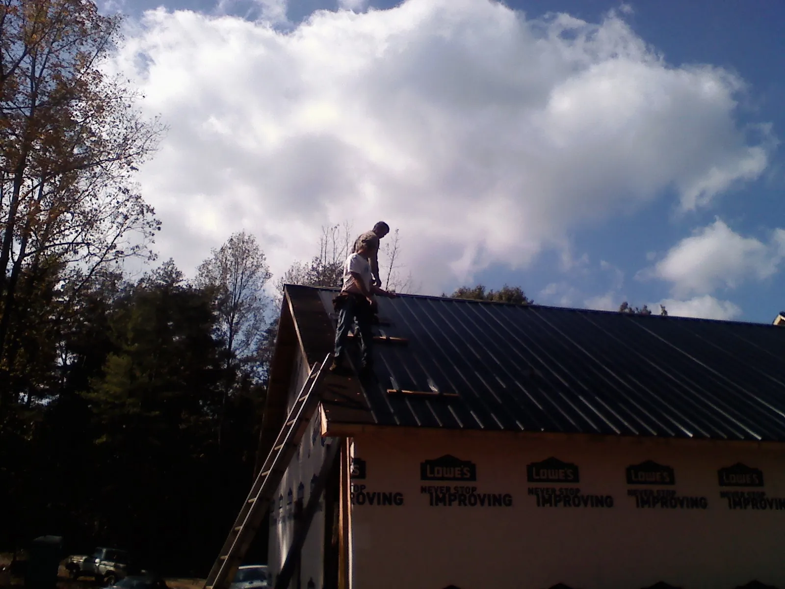 Roofer fastening dark metal panels high against a cloudy sky, from a Roof Inspection job in Clarks Grove
