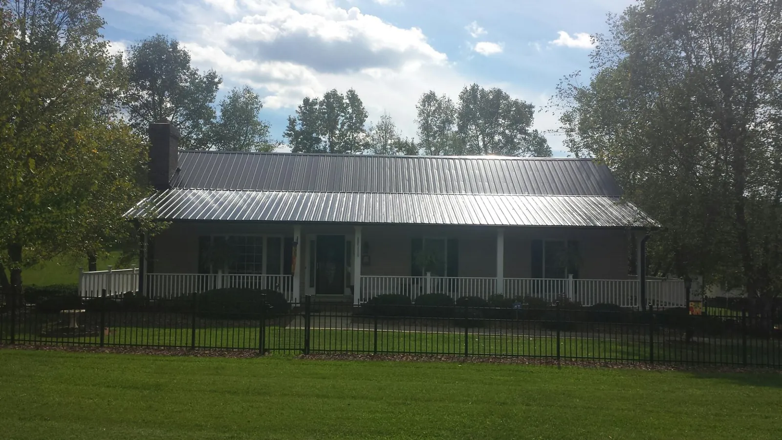 Gray metal roof on a brick ranch with a full width front porch — Gutter Guard Installation work by our crew in Clarks Grove