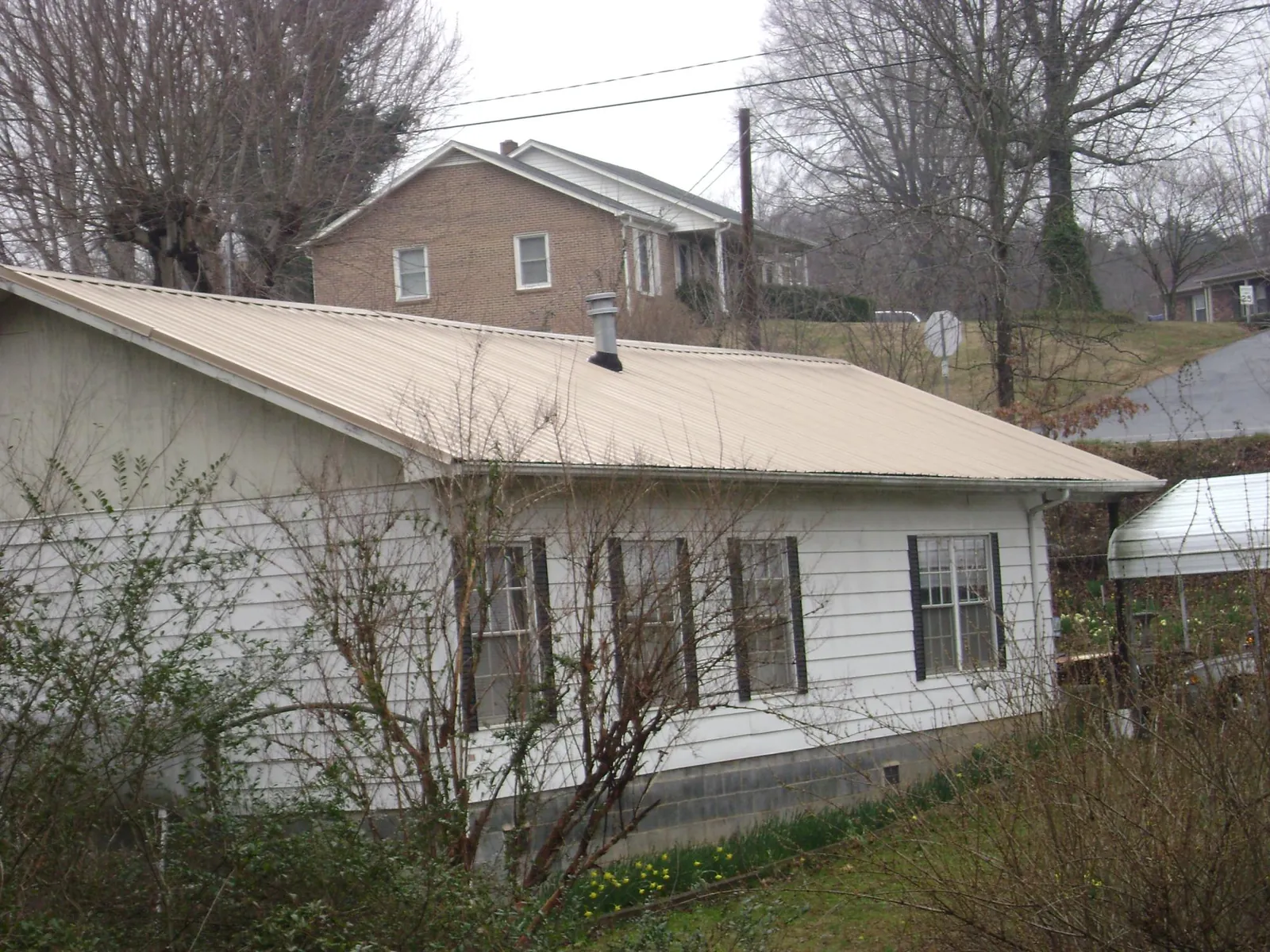Tan metal roof on a white sided house set into a hillside — Commercial Roofing by Roofing Brothers in Clarks Grove